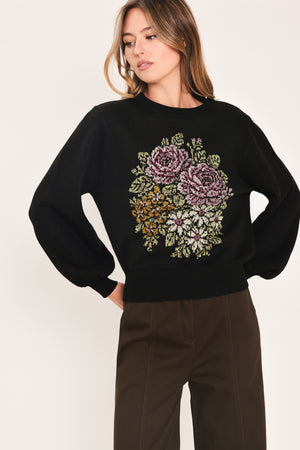A woman modeling a black crewneck sweatshirt featuring a large embroidered floral design in purple, green, and gold on the front | Flying Tomato