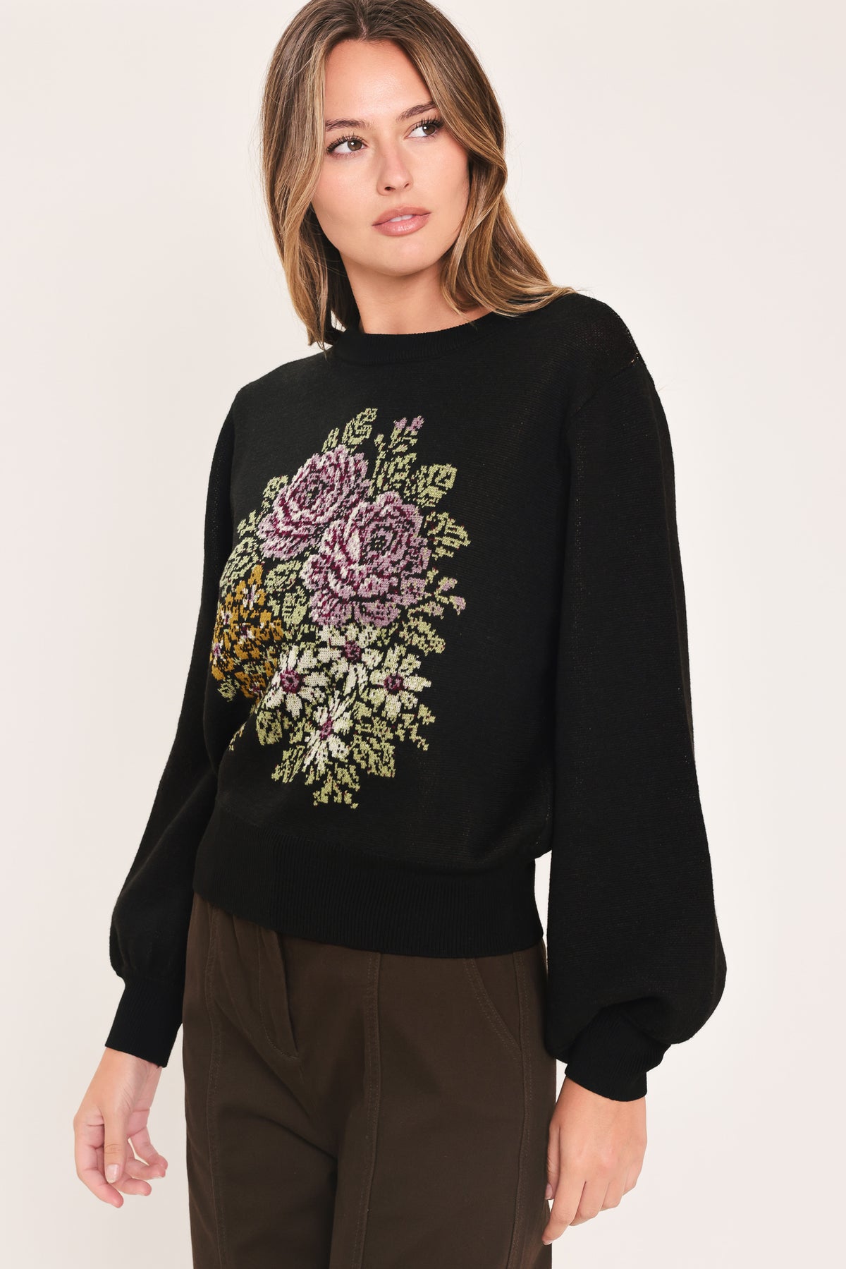 A woman modeling a black crewneck sweatshirt featuring a large embroidered floral design in purple, green, and gold on the front | Flying Tomato