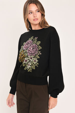 A woman modeling a black crewneck sweatshirt featuring a large embroidered floral design in purple, green, and gold on the front | Flying Tomato