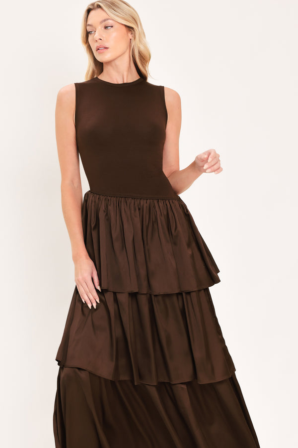 A woman modeling a sleeveless, high-neck, tiered skirt maxi dress in a deep chocolate brown color with an asymmetrical drop waist | Flying Tomato