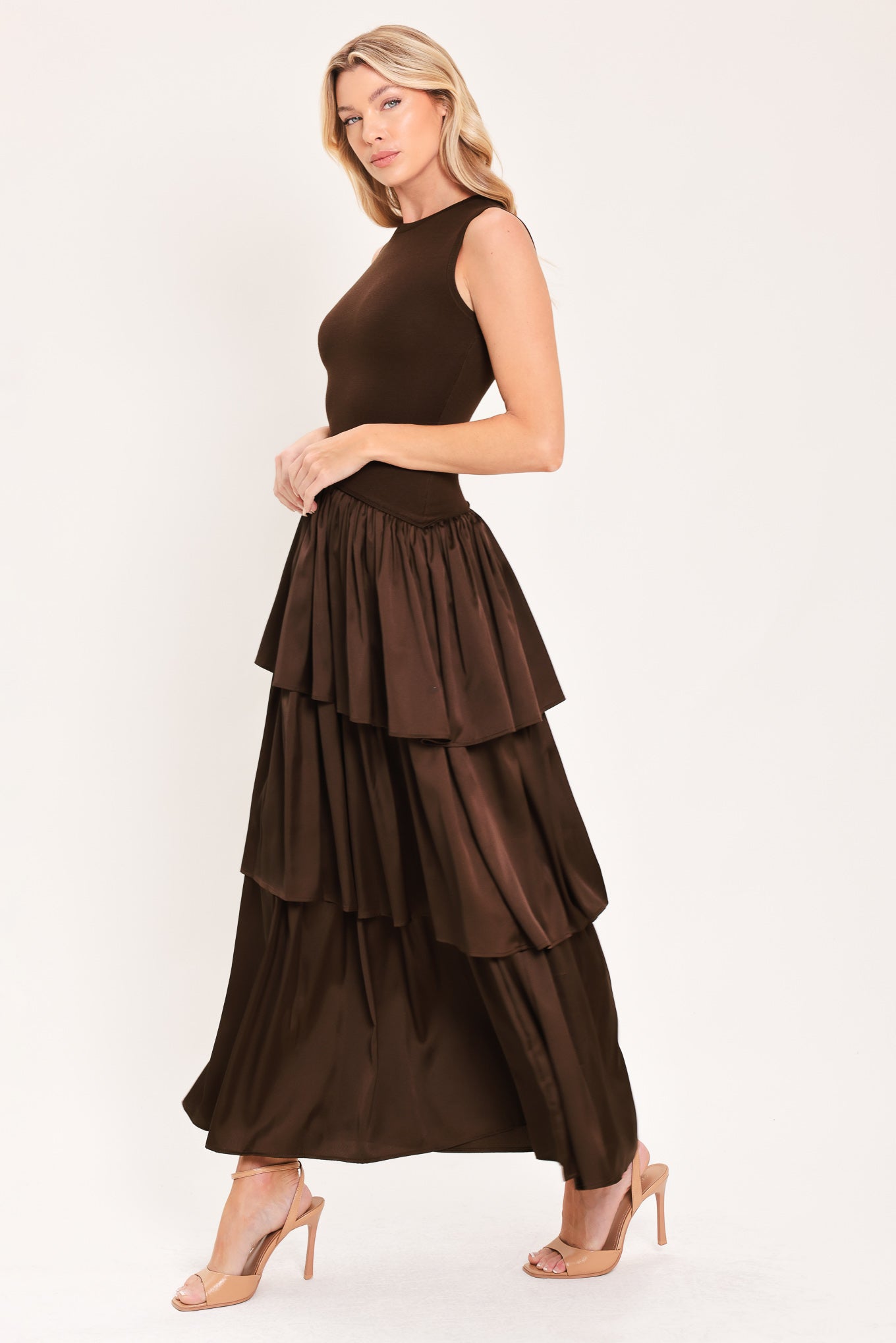 A woman modeling a sleeveless, high-neck, tiered skirt maxi dress in a deep chocolate brown color with an asymmetrical drop waist | Flying Tomato