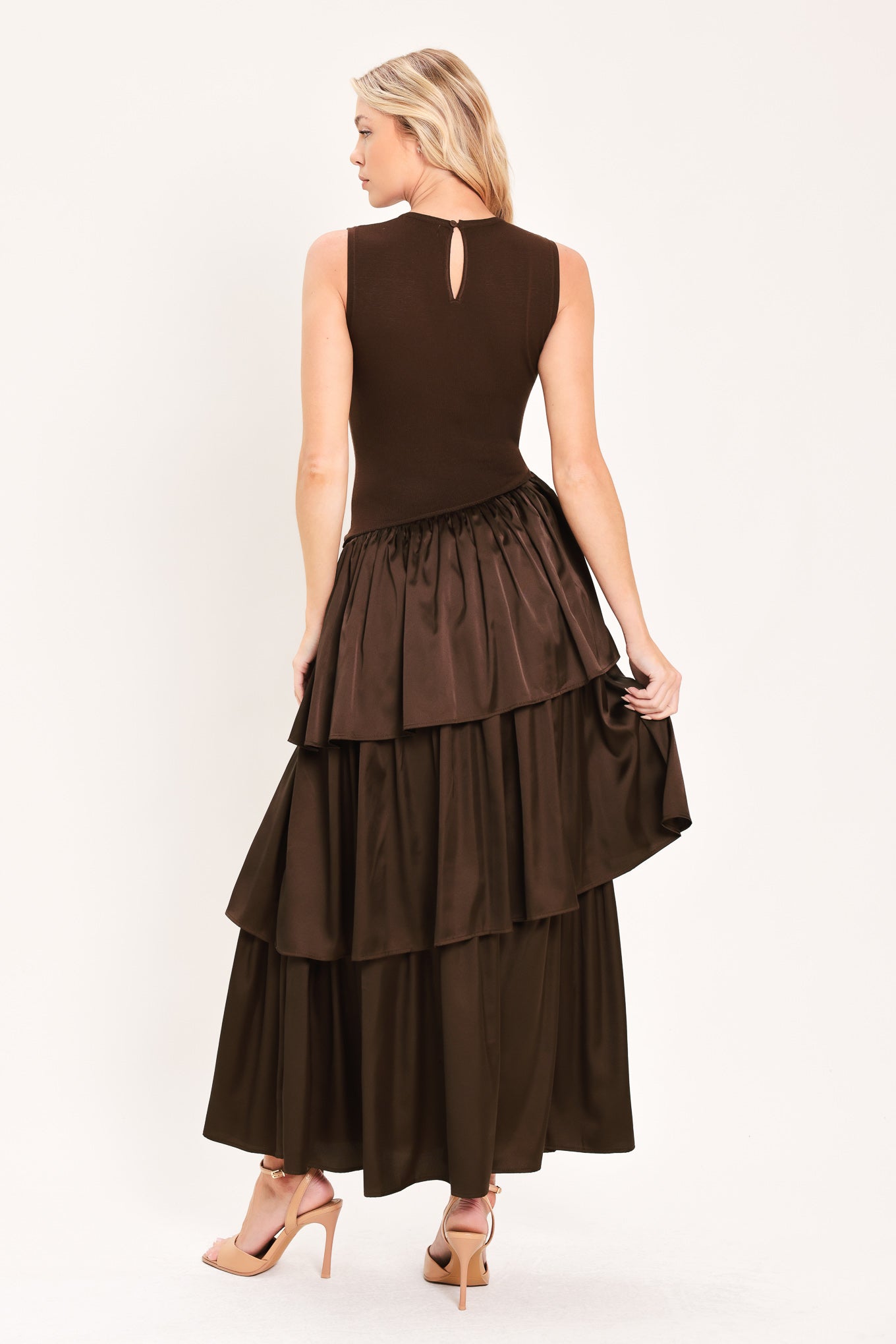 A woman modeling a sleeveless, high-neck, tiered skirt maxi dress in a deep chocolate brown color with an asymmetrical drop waist | Flying Tomato
