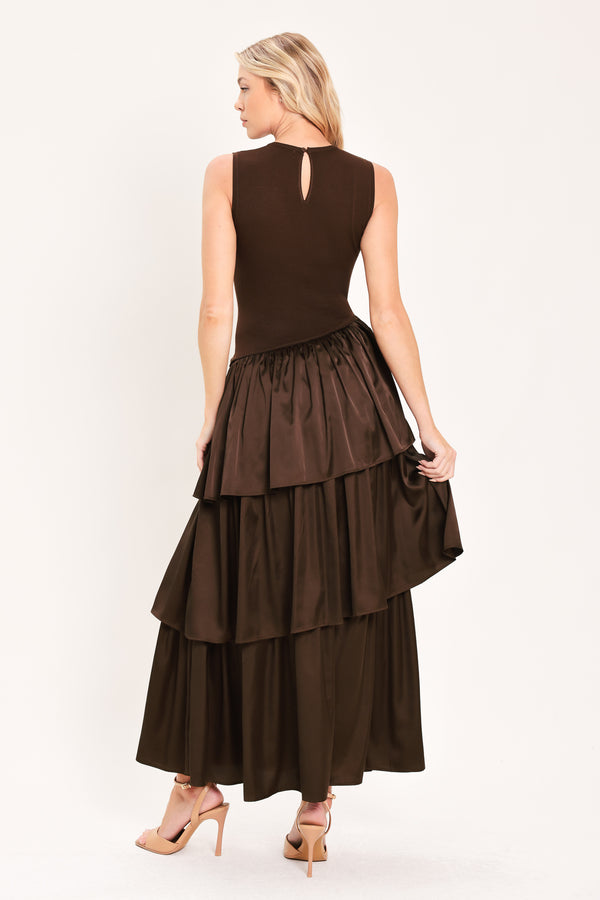 A woman modeling a sleeveless, high-neck, tiered skirt maxi dress in a deep chocolate brown color with an asymmetrical drop waist | Flying Tomato