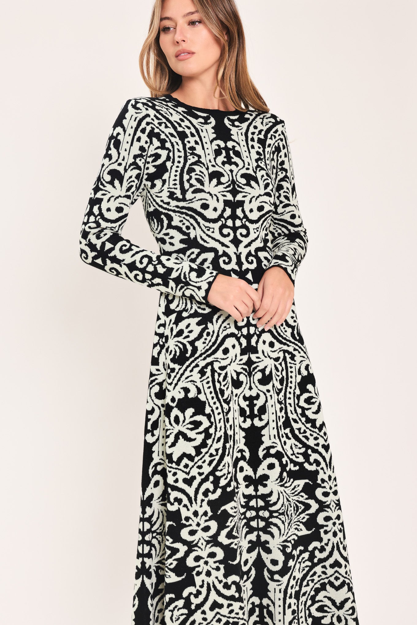 A woman modeling a long-sleeve midi dress with an intricate black and white damask pattern | Flying Tomato