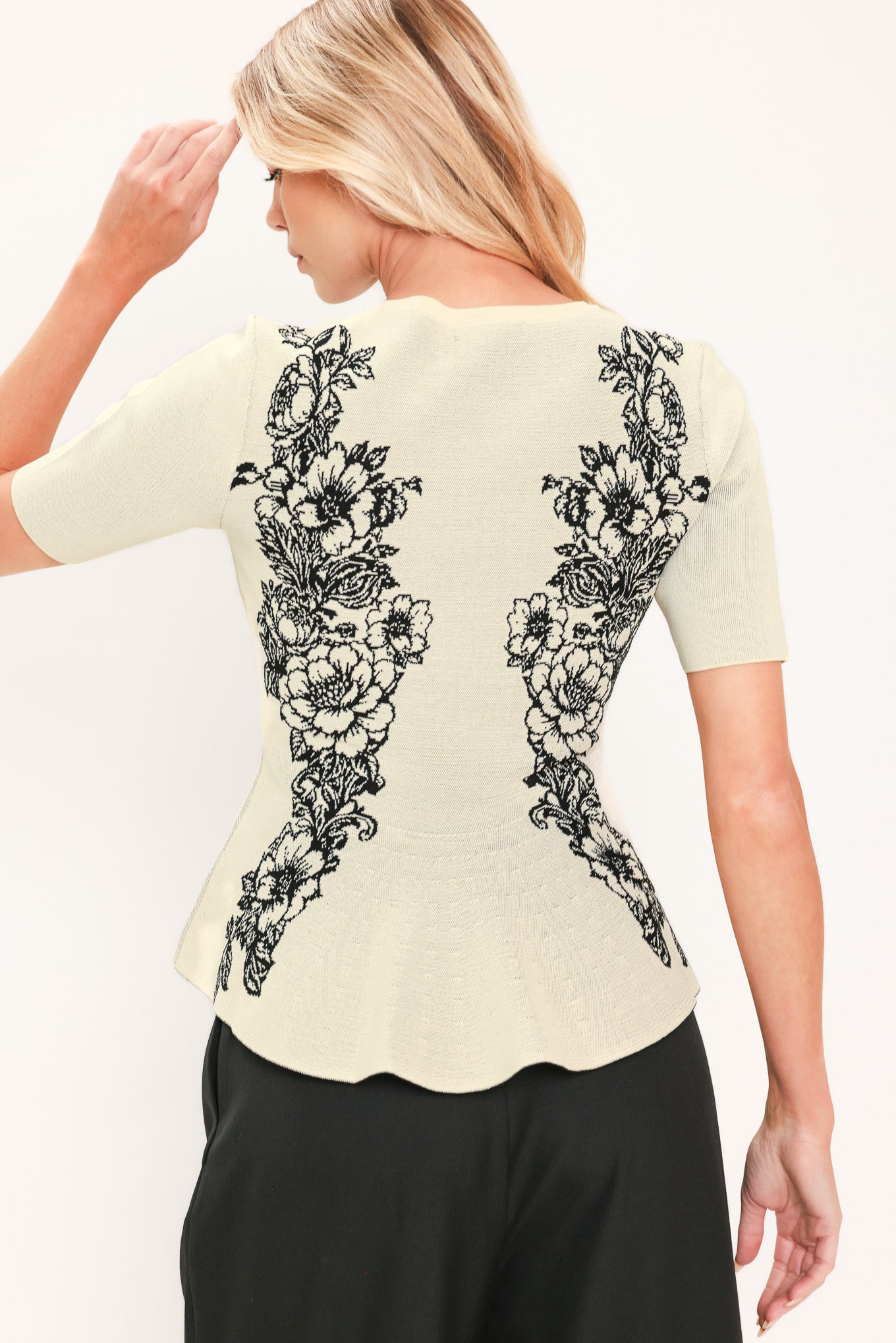 A woman modeling a cream-colored short-sleeve peplum top with black floral embroidery down the front | Flying Tomato