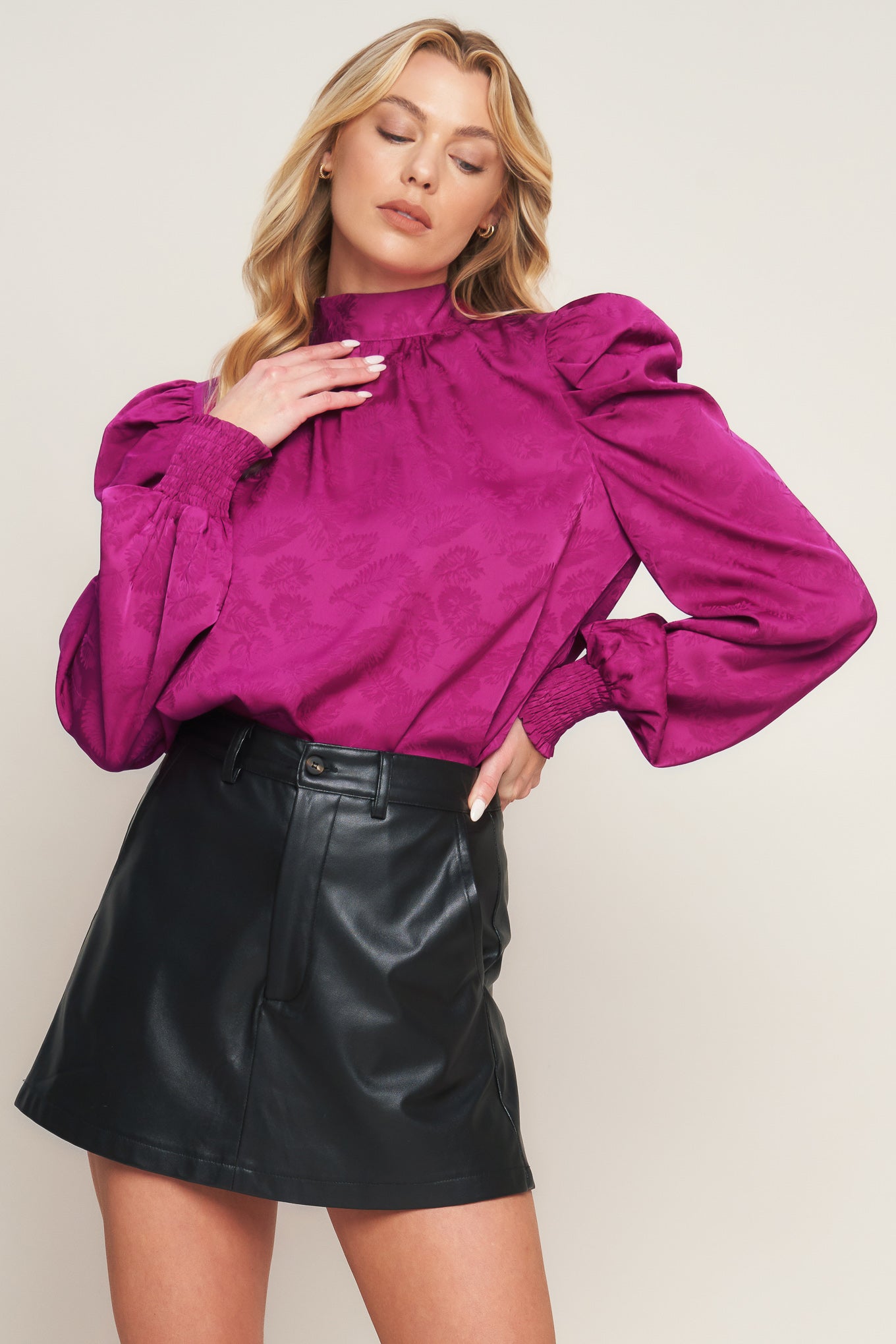 A satin top featuring high neckline, long puff sleeve with smocked cuff and back sash tie closure
