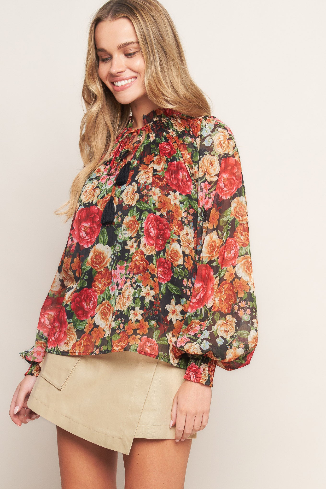 A printed woven top featuring high neckline, peasant sleeve with smocked cuff and front tie detail