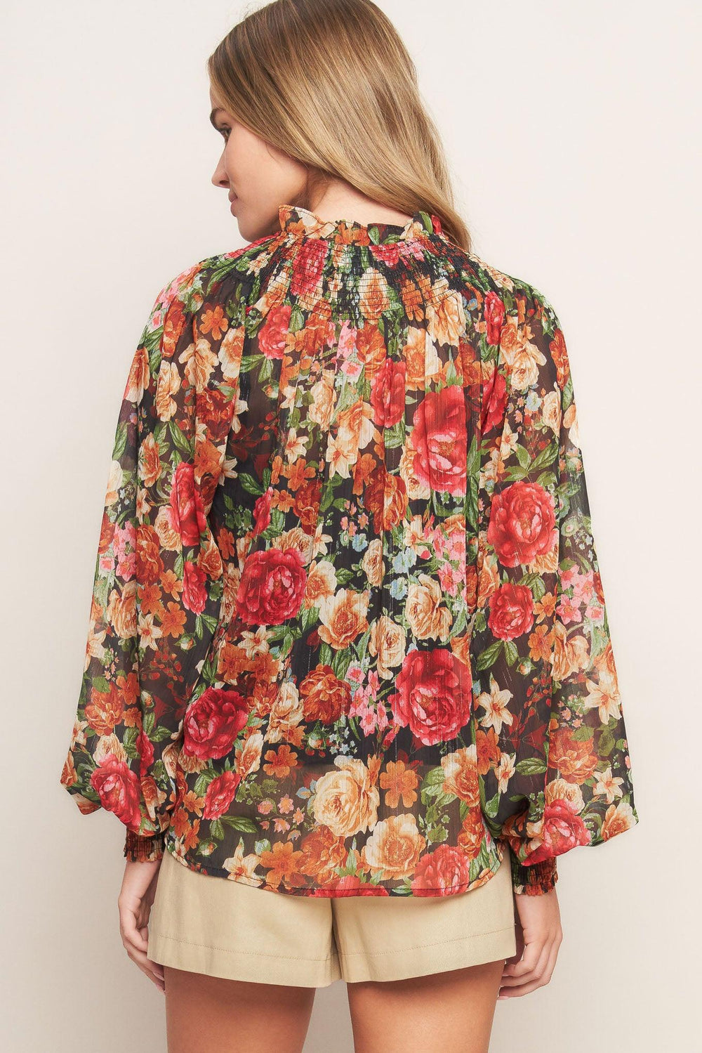 A printed woven top featuring high neckline, peasant sleeve with smocked cuff and front tie detail