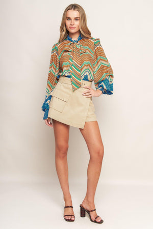 A printed woven top featuring high neckline with back neck tie and long sleeve with smocked cuff
