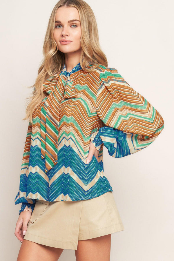 A printed woven top featuring high neckline with back neck tie and long sleeve with smocked cuff