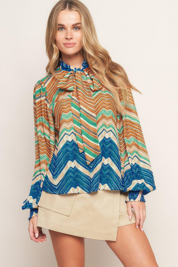 A printed woven top featuring high neckline with back neck tie and long sleeve with smocked cuff