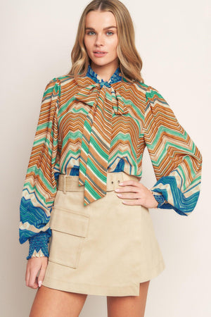 A printed woven top featuring high neckline with back neck tie and long sleeve with smocked cuff