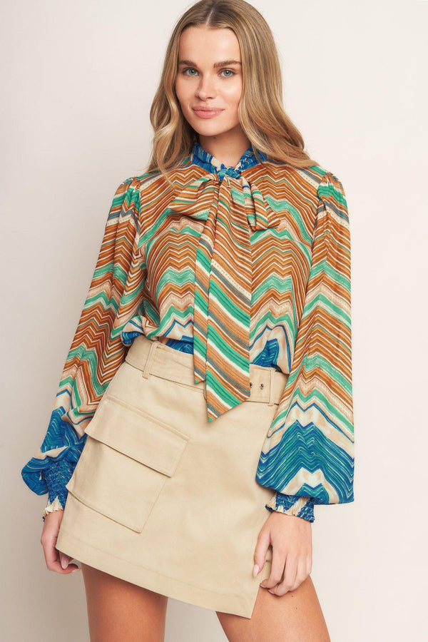 A printed woven top featuring high neckline with back neck tie and long sleeve with smocked cuff