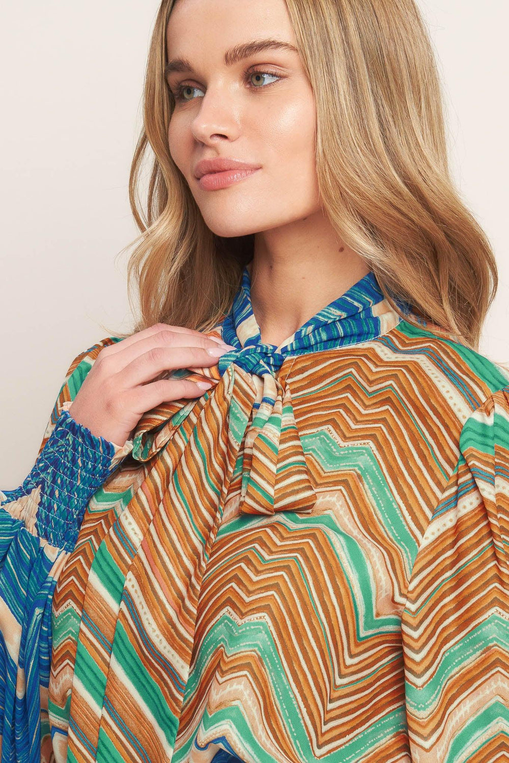 A printed woven top featuring high neckline with back neck tie and long sleeve with smocked cuff