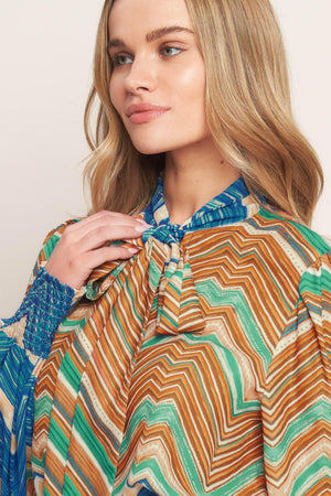 A printed woven top featuring high neckline with back neck tie and long sleeve with smocked cuff