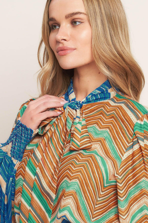 A printed woven top featuring high neckline with back neck tie and long sleeve with smocked cuff