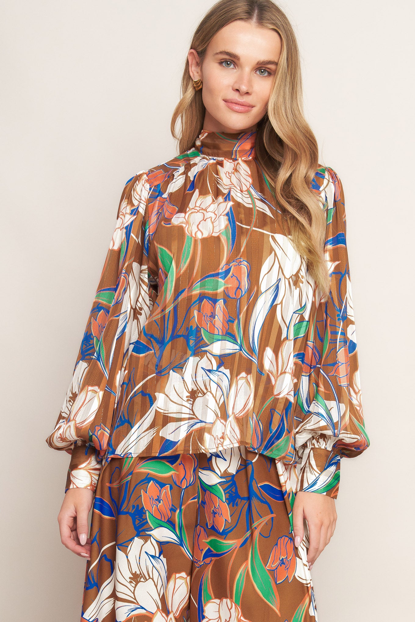 A printed woven top featuring a high neckline, blouson sleeve with cuff, and back neck tie closure.