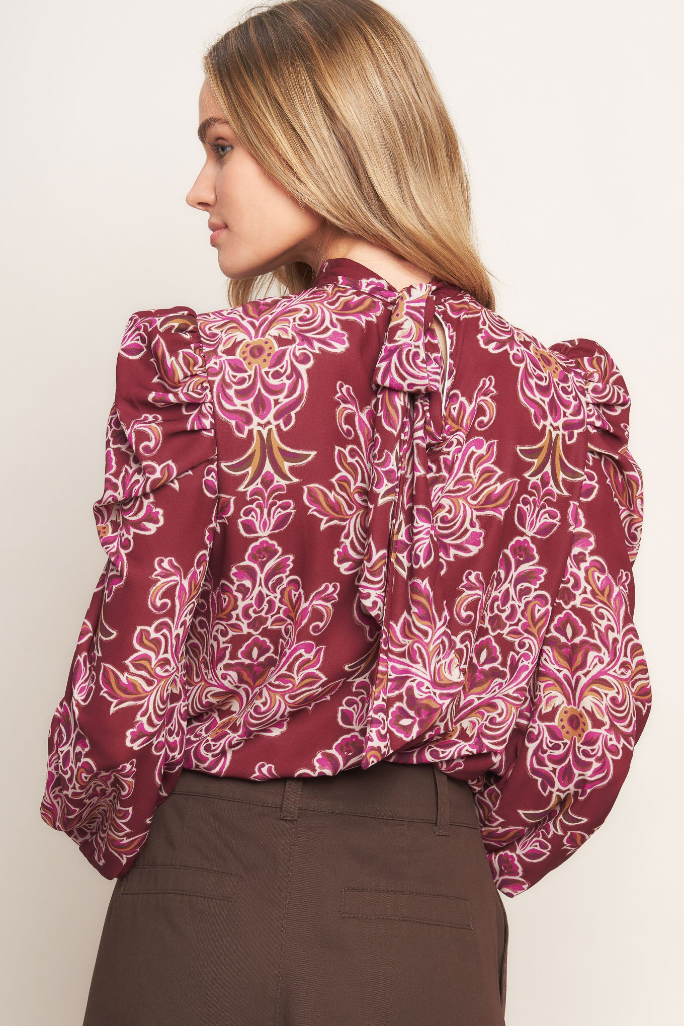 A printed woven top featuring high neckline, long puff sleeve and back neck tie closure