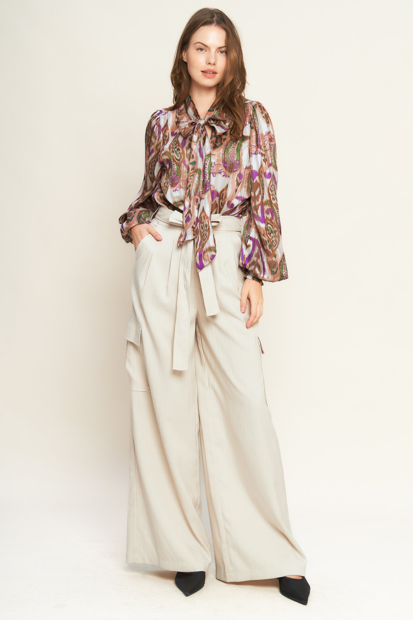 Woman wearing a patterned blouse with a bow tie against a plain background. A printed woven top featuring front bow tie and long sleeve with smocked cuff - FLYING TOMATO