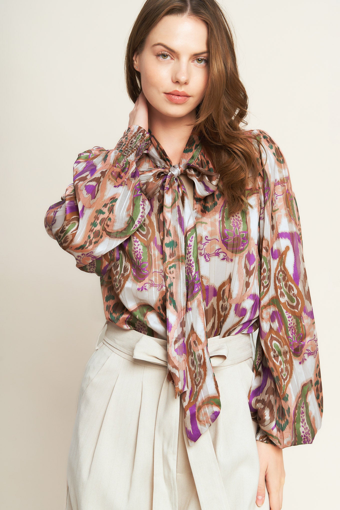 Woman wearing a patterned blouse with a bow tie against a plain background. A printed woven top featuring front bow tie and long sleeve with smocked cuff - FLYING TOMATO