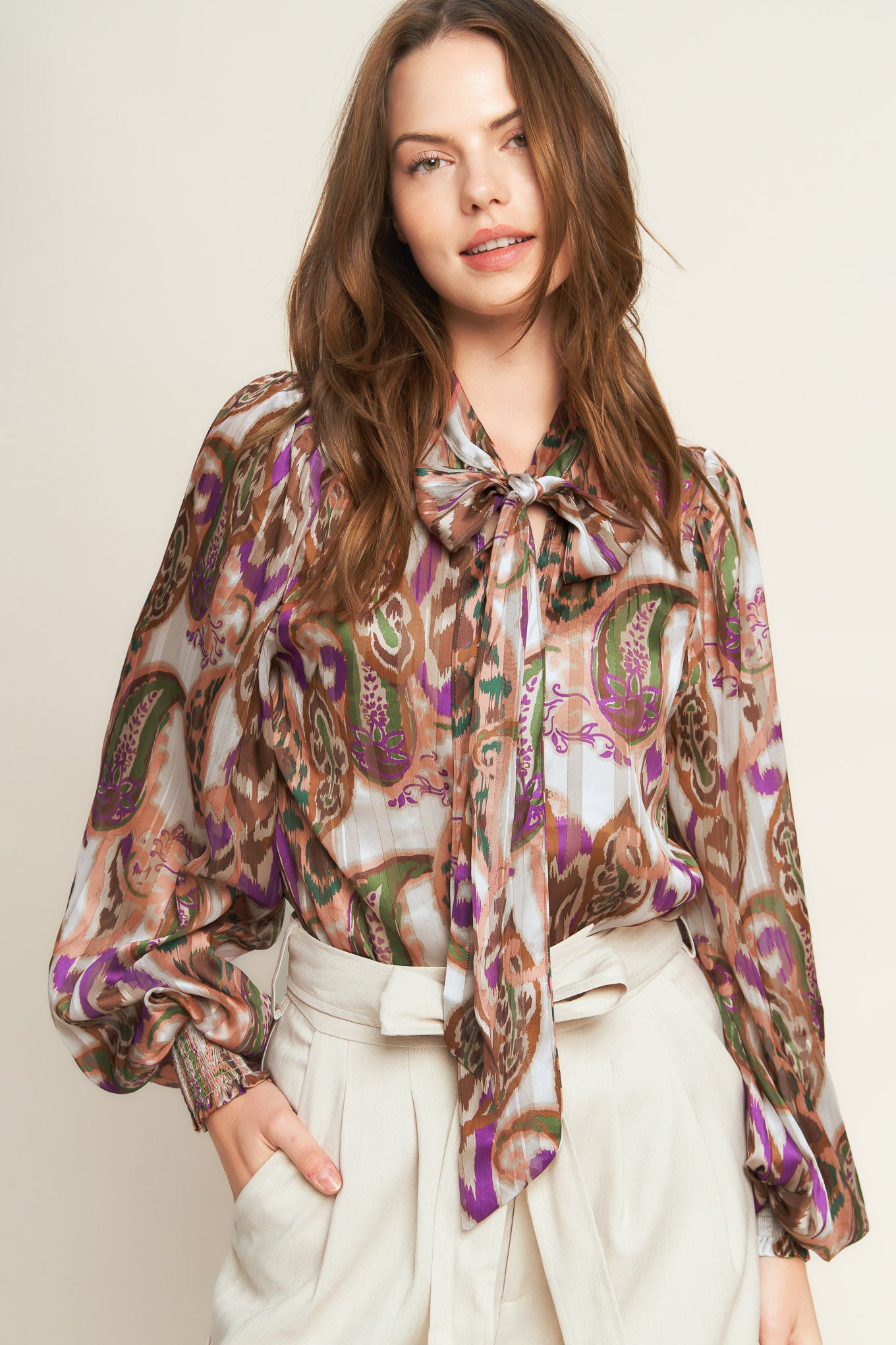 Woman wearing a patterned blouse with a bow tie against a plain background. A printed woven top featuring front bow tie and long sleeve with smocked cuff - FLYING TOMATO