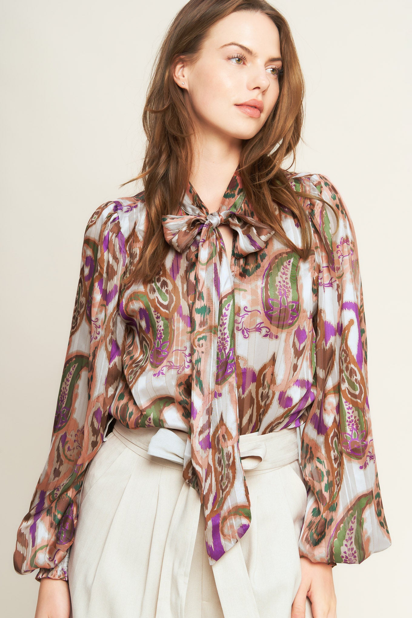 Woman wearing a patterned blouse with a bow tie against a plain background. A printed woven top featuring front bow tie and long sleeve with smocked cuff - FLYING TOMATO