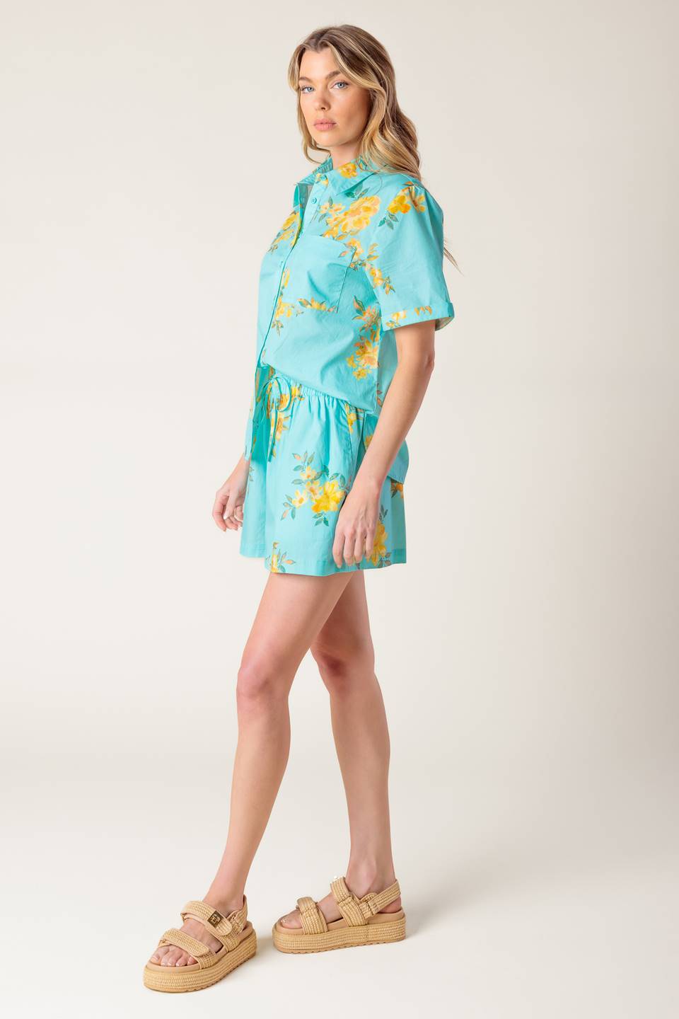 A printed turquoise woven top and short set. Top featuring yellow floral print, collar, cuffed short sleeve and button down. Short featuring elasticized waistband with front tie.