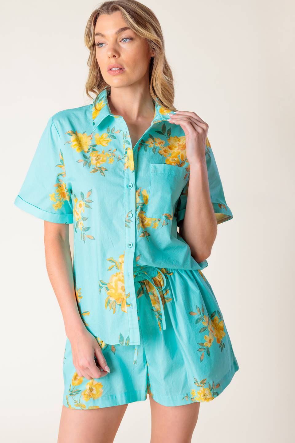 A printed turquoise woven top and short set. Top featuring yellow floral print, collar, cuffed short sleeve and button down. Short featuring elasticized waistband with front tie.