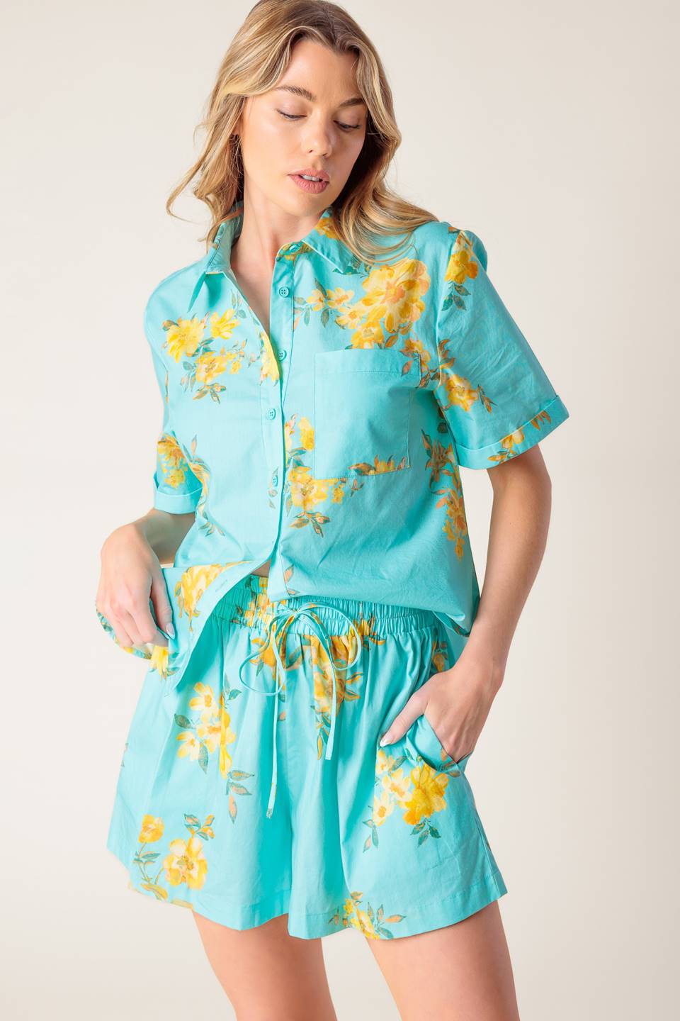 A printed turquoise woven top and short set. Top featuring yellow floral print, collar, cuffed short sleeve and button down. Short featuring elasticized waistband with front tie.