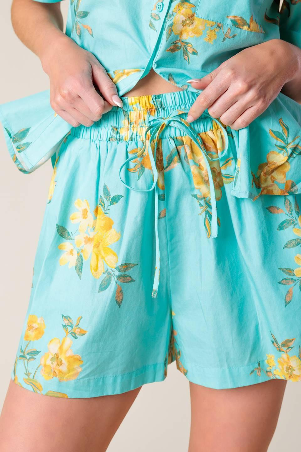 A printed turquoise woven top and short set. Top featuring yellow floral print, collar, cuffed short sleeve and button down. Short featuring elasticized waistband with front tie.