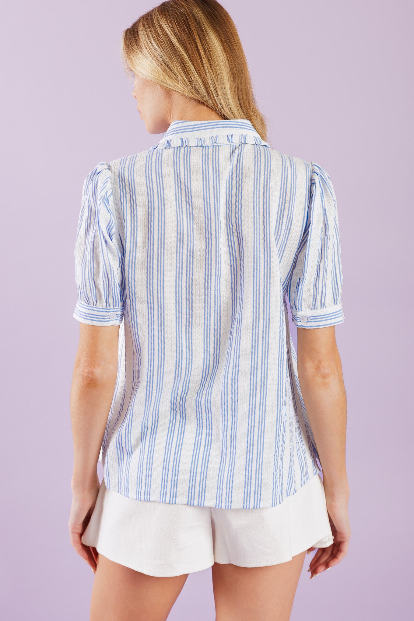 This woven top showcases a classic blue and white striped pattern, complete with a ruffled collar, cuffed short sleeves, and lace inset detailing. The button down front adds a touch of sophistication to the garment.