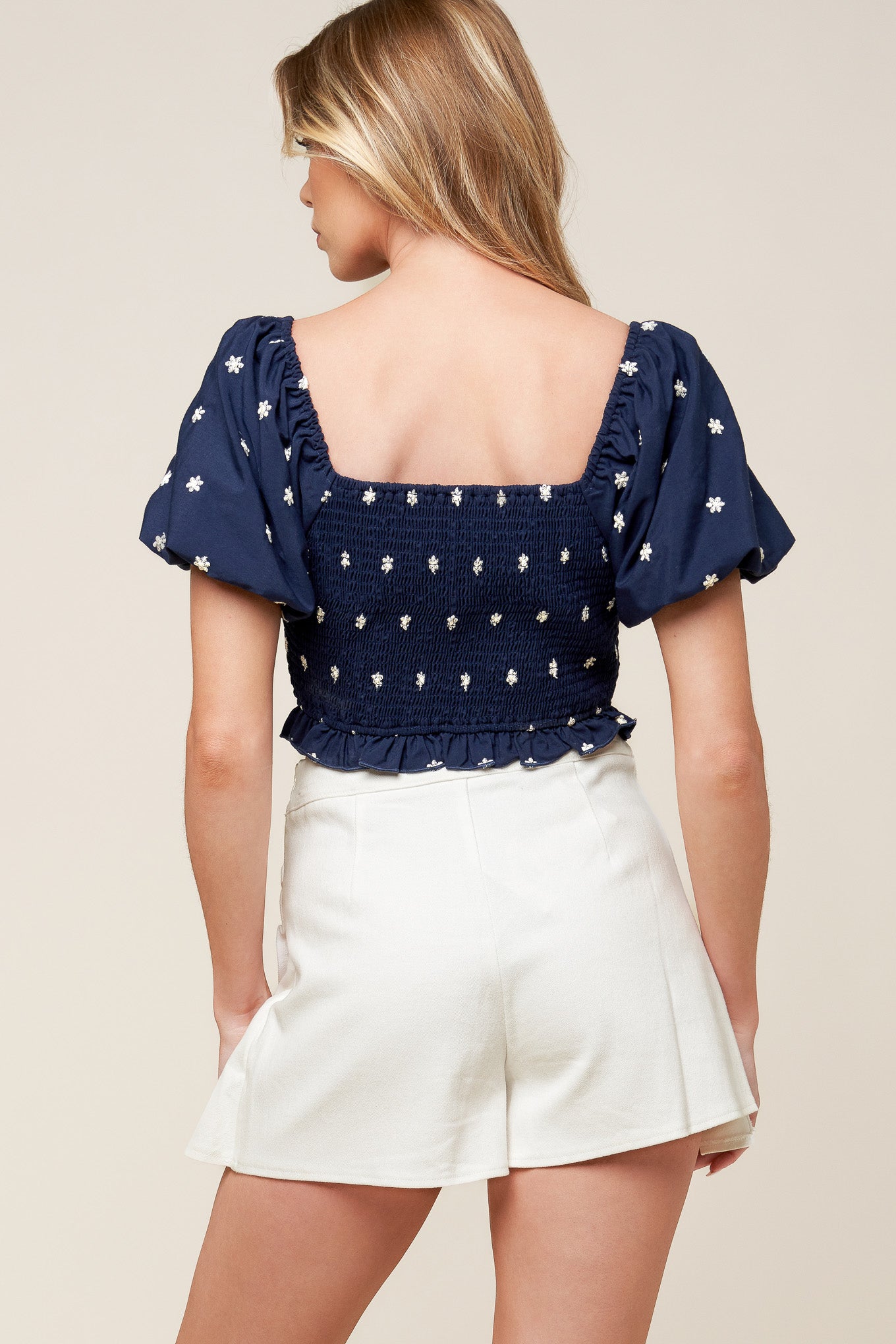 A solid embroidered woven top featuring sweetheart neckline, short sleeve, gathered center front, ruffled hemline and smocked back bodice.