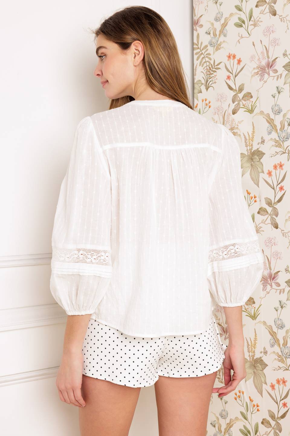 A solid textured woven top featuring china collar, 3/4 sleeve, button down and lace inset with pleats.