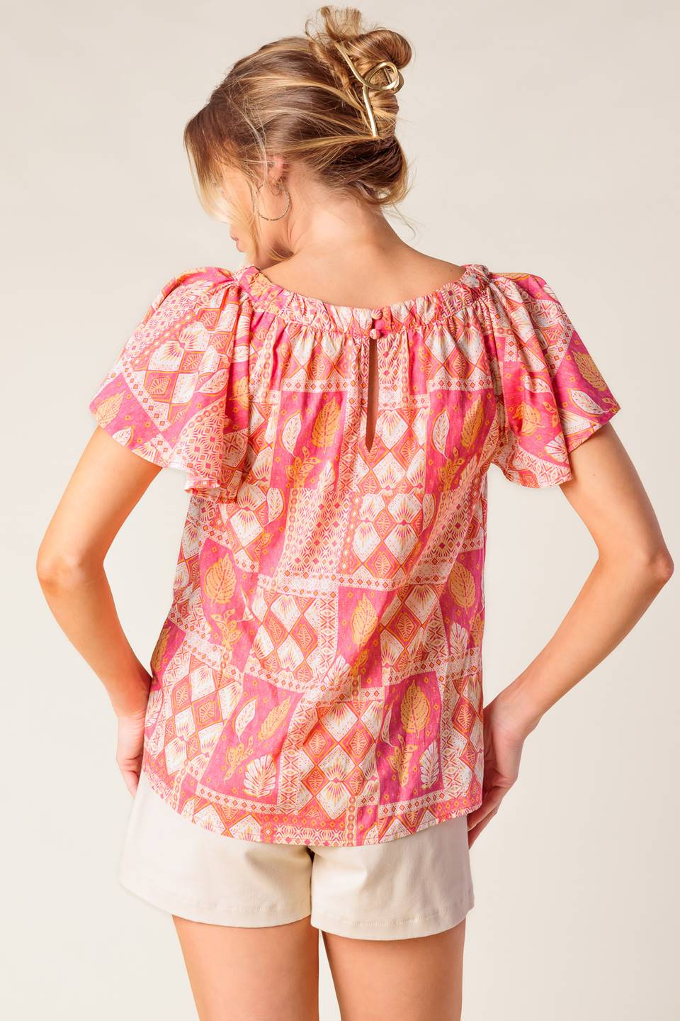 A printed woven top featuring round neckline, flutter sleeve and back neck button closure