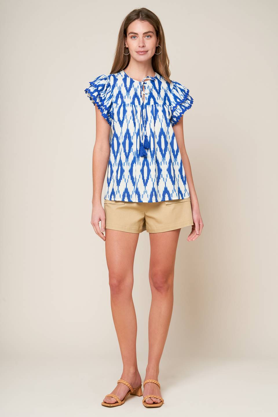 A printed woven top featuring round neckline with front tie and double layer short sleeve with ric rac ribbon trim.