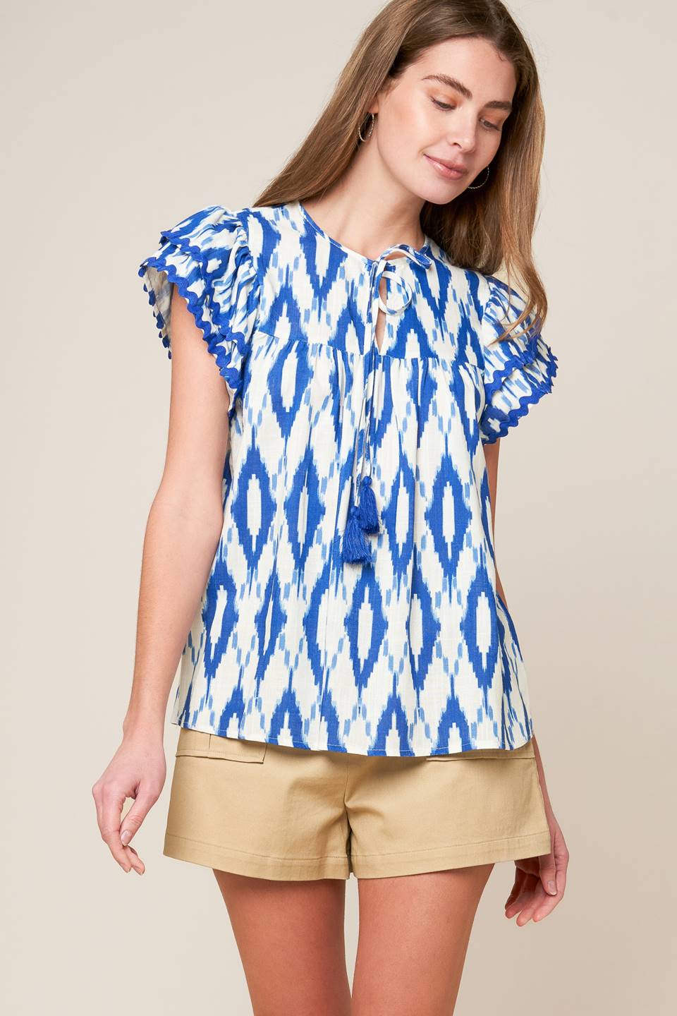 A printed woven top featuring round neckline with front tie and double layer short sleeve with ric rac ribbon trim.