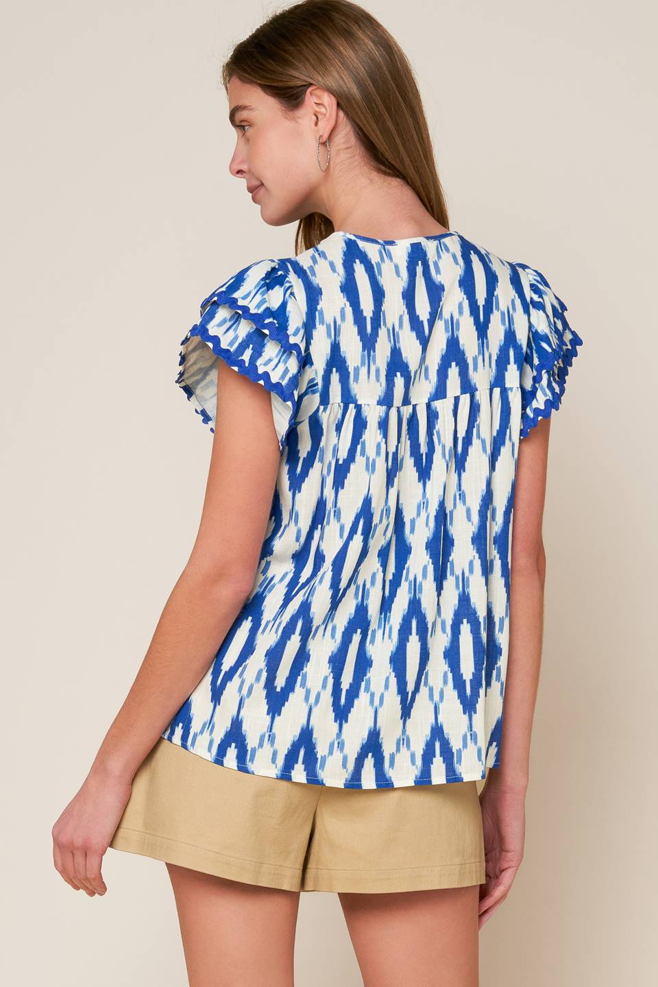 A printed woven top featuring round neckline with front tie and double layer short sleeve with ric rac ribbon trim.