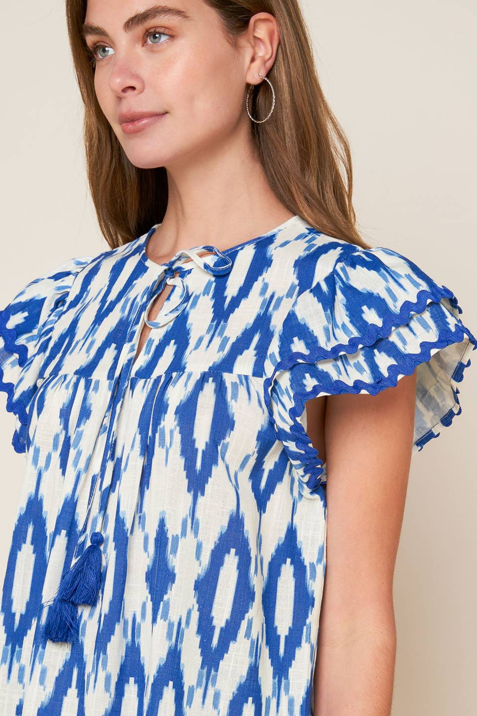 A printed woven top featuring round neckline with front tie and double layer short sleeve with ric rac ribbon trim.