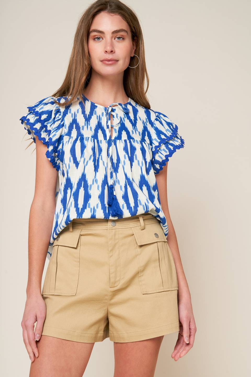 A printed woven top featuring round neckline with front tie and double layer short sleeve with ric rac ribbon trim.