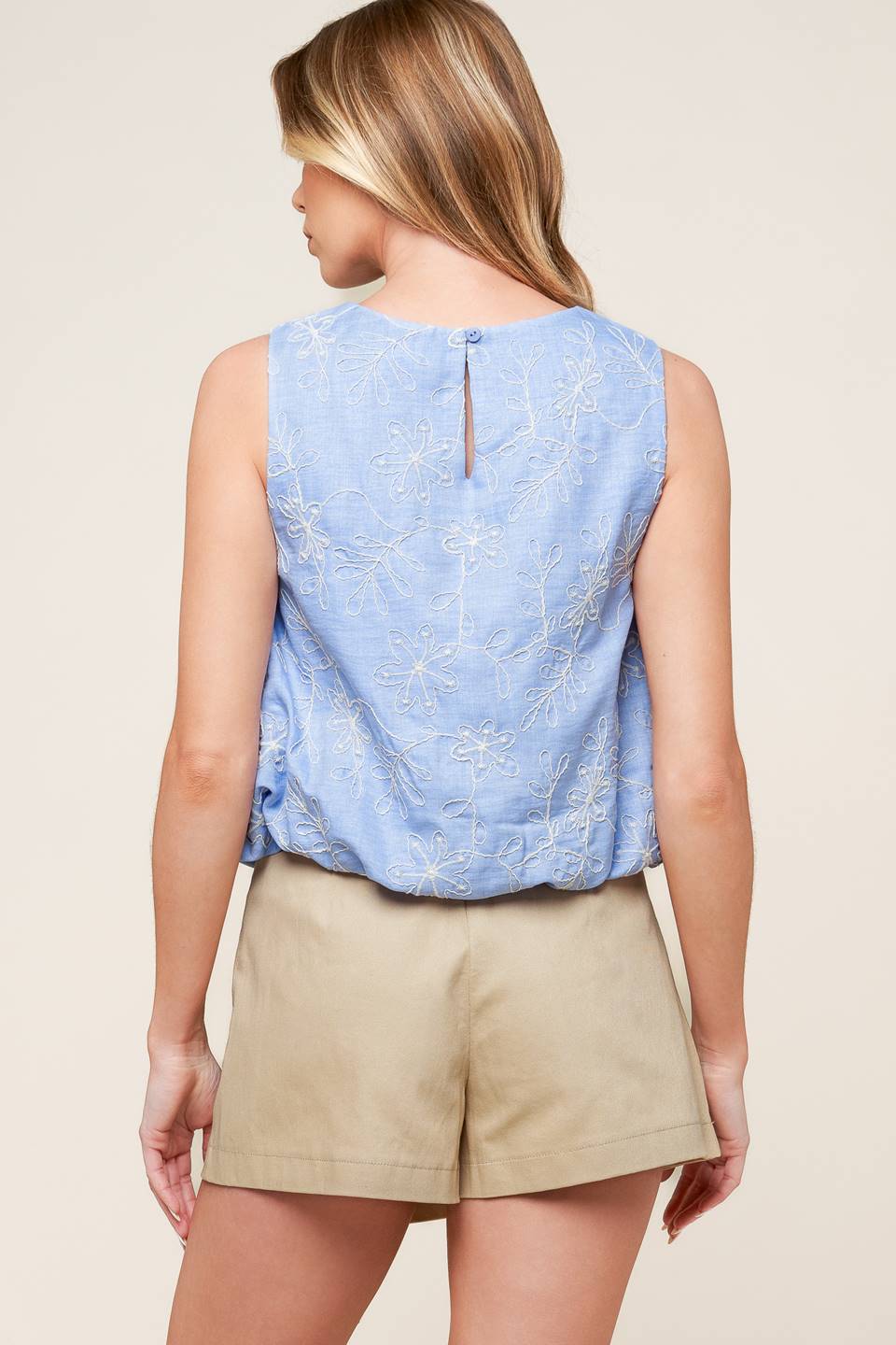 A sleeveless, solid blue embroidered top with elasticized waist and back button closure.