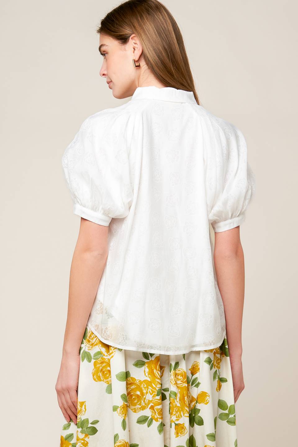 A white textured woven top featuring raglan sleeves and embellished button down.