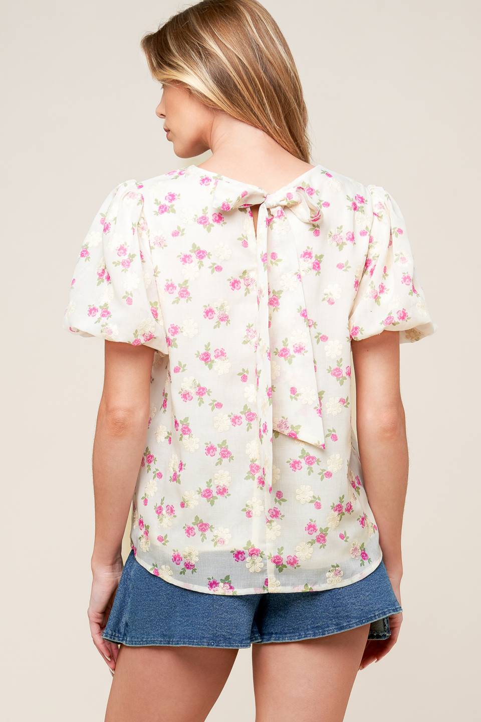 A textured floral printed woven top featuring round neckline, short balloon sleeves and back neck tie closure.