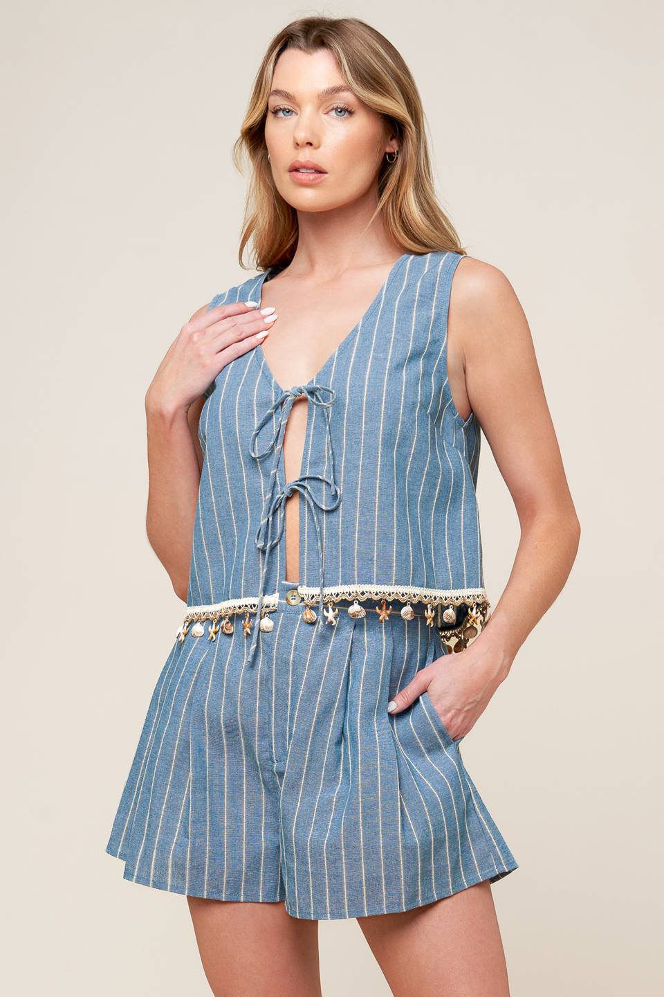 A striped woven top and shorts set. Top featuring front bow ties, sleeveless and seashell trimmed hem. Shorts featuring front closure and side pockets