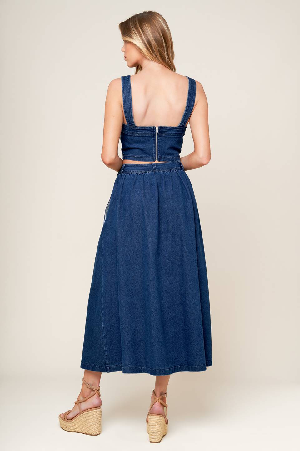 A washed denim top and skirt set. Top featuring cropped length, straight neckline, strap and back zipper closure. Skirt featuring full skirt with front button closure.