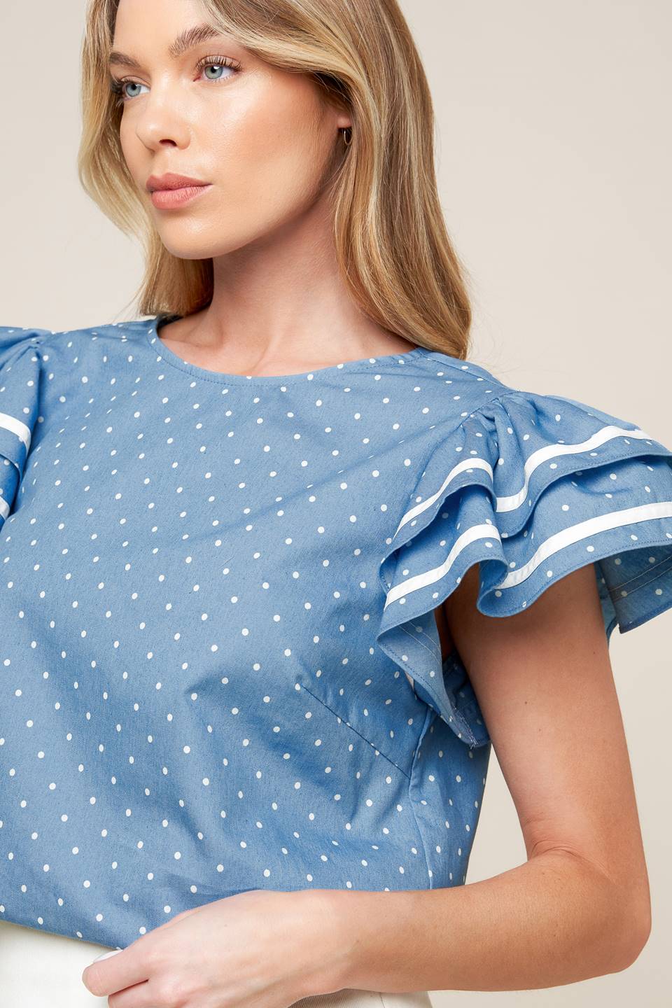 A printed woven top featuring round neckline, double ruffled sleeves and back neck button closure.