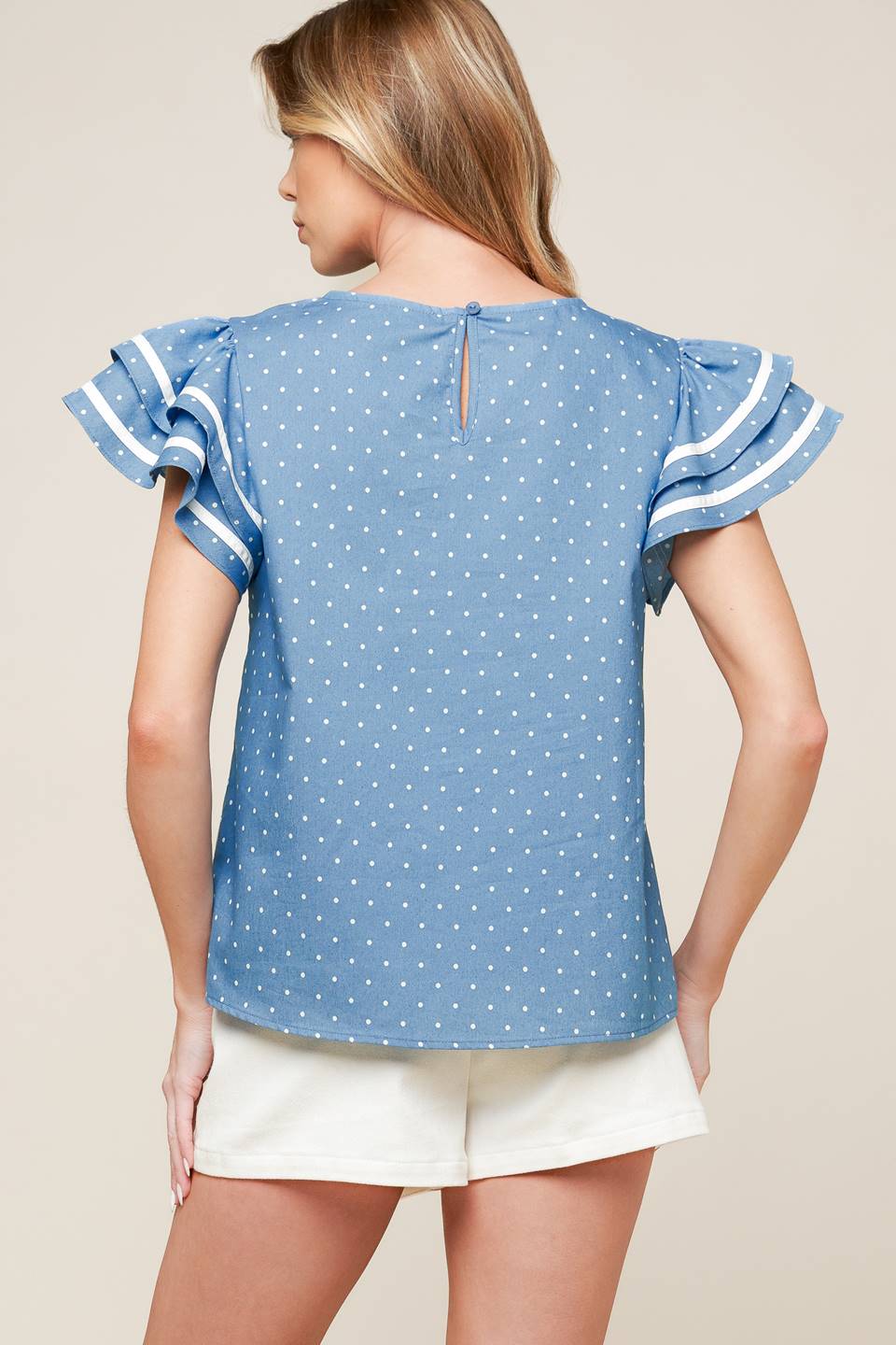 A printed woven top featuring round neckline, double ruffled sleeves and back neck button closure.