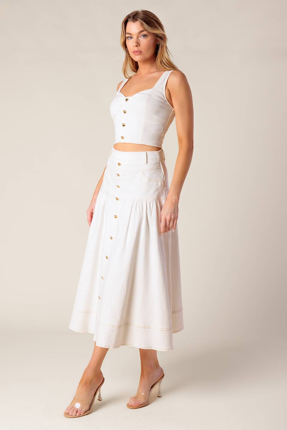 A solid white woven top and skirt set. Top featuring bustier top with front button detail and back zipper closure. Skirt featuring front button down detail and back zipper closure