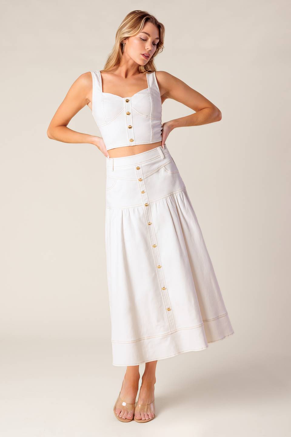 A solid white woven top and skirt set. Top featuring bustier top with front button detail and back zipper closure. Skirt featuring front button down detail and back zipper closure