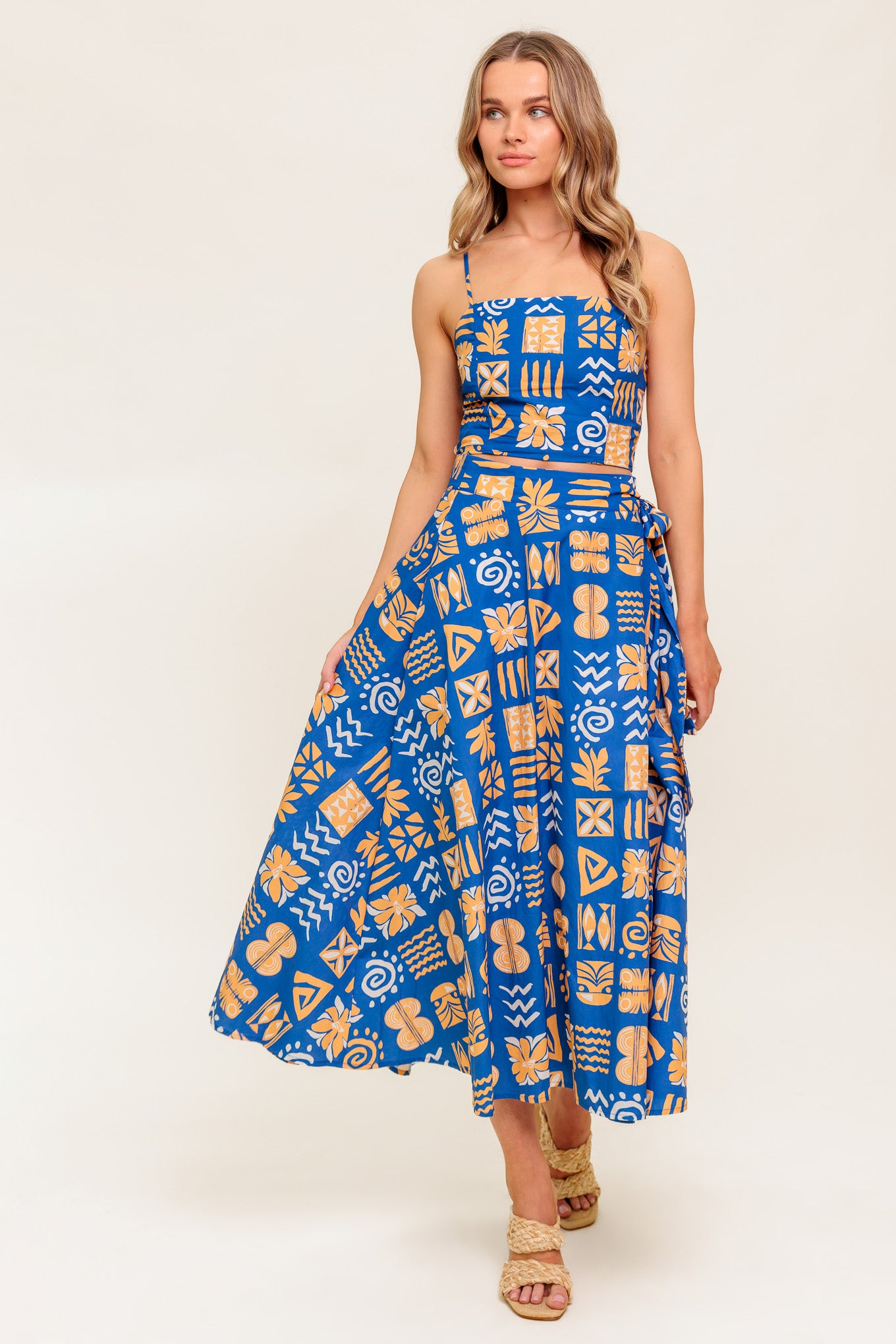 A printed woven top and skirt set. Crop top featuring straight neckline, straps and smocked back bodice. True wrap skirt with side tie