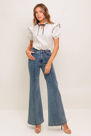 A solid woven top featuring ruffed neckline with tie, scallop edge shoulder and short sleeve